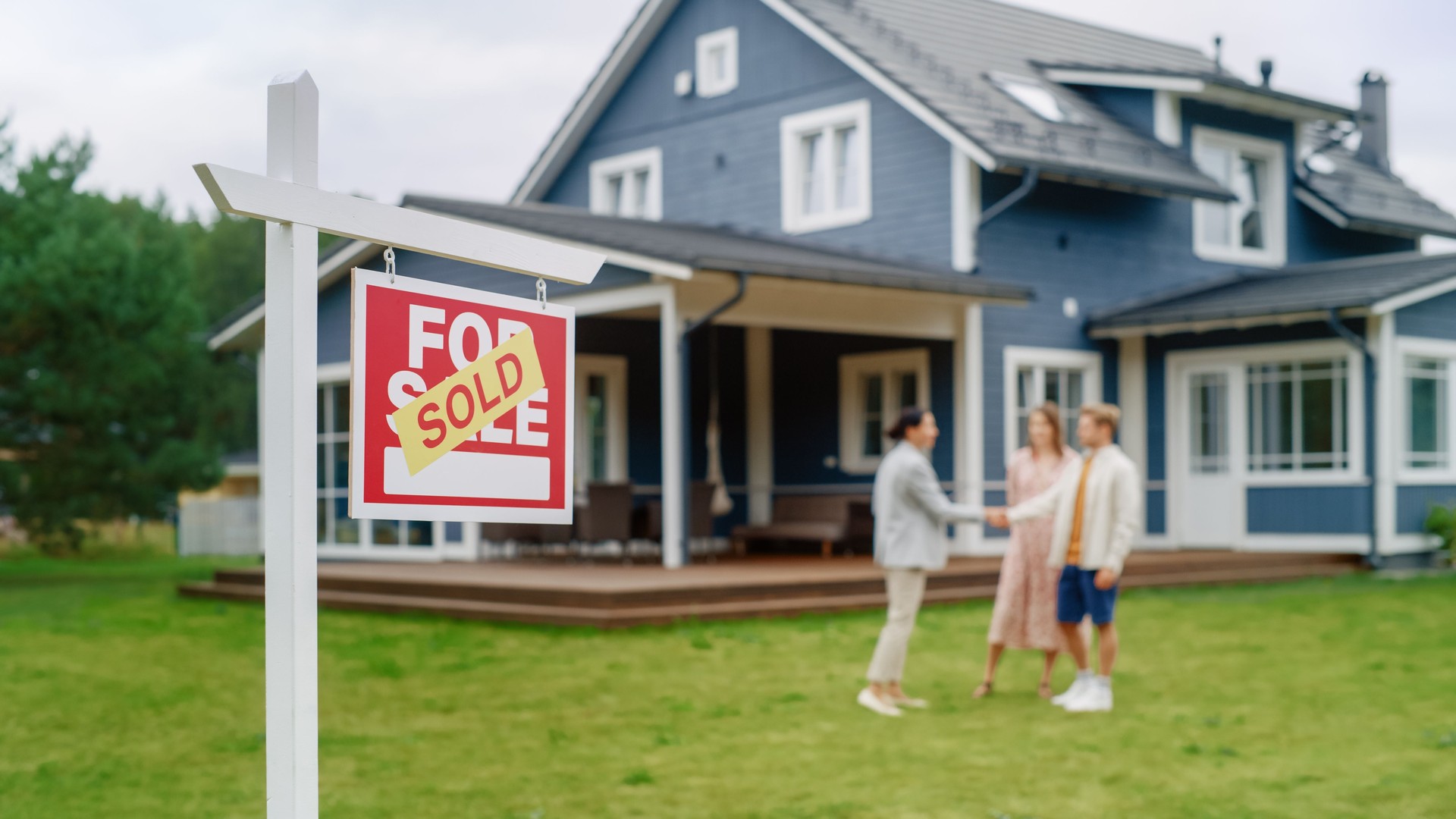 Young Couple Visiting a Potential New Home Property , SHaking Hands with Professional Real Estate Agent. Female real estate agent Showing the Area to Future Homeowners. Focus on Sold Sign.